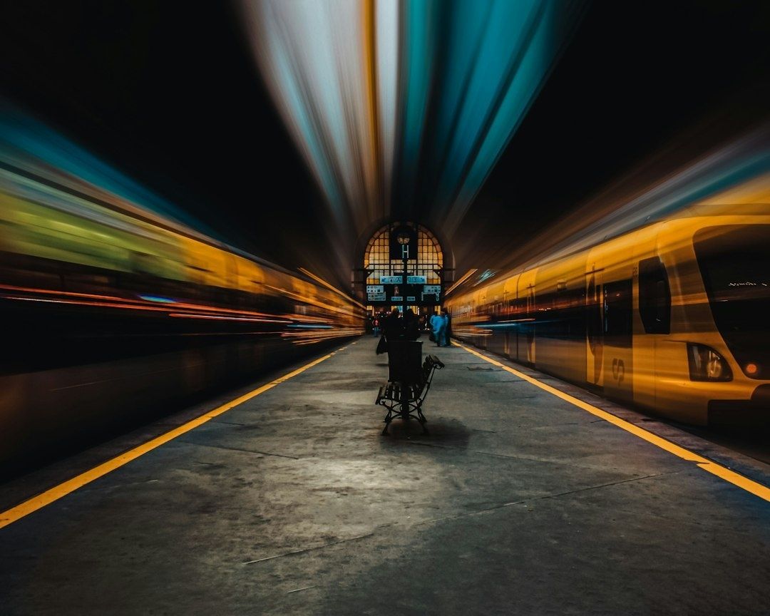 Cykelvagn på perrong mellan två suddiga tåg i kvällsljus